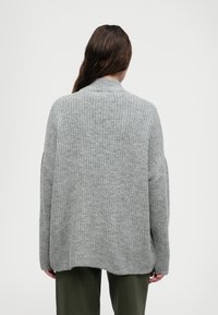 Γκρίζα πλεκτή ζακέτα με υφή, διαθέτοντας ψηλό λαιμό, χαμηλούς ώμους και άνετη εφαρμογή, που επεκτείνεται πέρα από τους γοφούς.