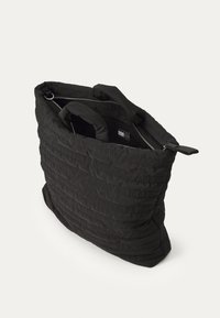 Black quilted tote bag with embossed logo pattern, featuring dual handles and a zip closure. Soft texture and structured design.