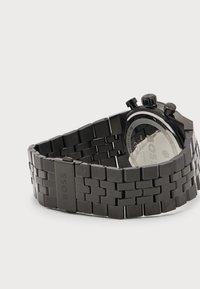 Ρολόι χειρός με μαύρο μπρασελέ από μέταλλο, κουμπιά χρονογράφου, με σήμα "BOSS" στην πόρπη και πίσω μέρος από ανοξείδωτο ατσάλι, γωνιακό σε ανοιχτό φόντο.