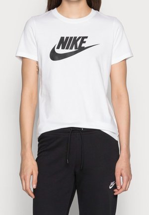 T-shirt blanc Nike avec un grand logo noir, porté avec un jogging noir Nike avec un petit logo blanc sur la cuisse.