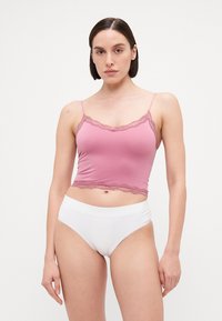 Camisole rose avec des bordures en dentelle, bretelles ajustables ; porté avec des culottes blanches taille haute. Tissu lisse, design ajusté, style basique.