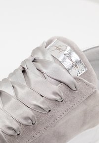 Jasnoszare zamszowe trampki z szerokimi satynowymi sznurówkami i błyszczącą srebrną metką na języku z napisanym kursywą logo marki.