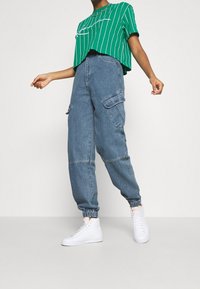 Grönrandig kortärmad t-shirt som är croppad, tillsammans med högmidjade denim cargo-byxor med elastiska muddarna och sidofickor. Vita sneakers.