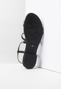 Sandal nera con suola in gomma piatta, dotata di sottili cinghie e design minimalista. Contrassegnata con il nome del marchio e la taglia 37.