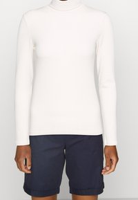 Vit långärmad polokrage i ribbat tyg, kombinerat med marinblå shorts. Toppen har en åtsittande design och en jämn yta.