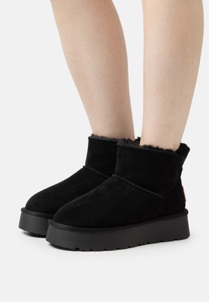 Stivaletti neri in suede con una morbida fodera simile alla pelliccia, dotati di una suola piatta nera e dettagli cuciti lungo le cuciture.