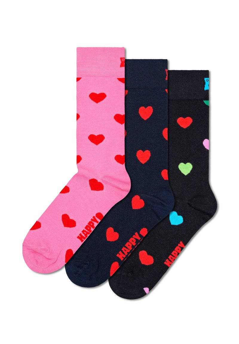 Trois paires de chaussettes en coton. La première est rose avec des cœurs rouges ; la deuxième est bleu marine avec des cœurs rouges ; la troisième est noire avec des cœurs multicolores.