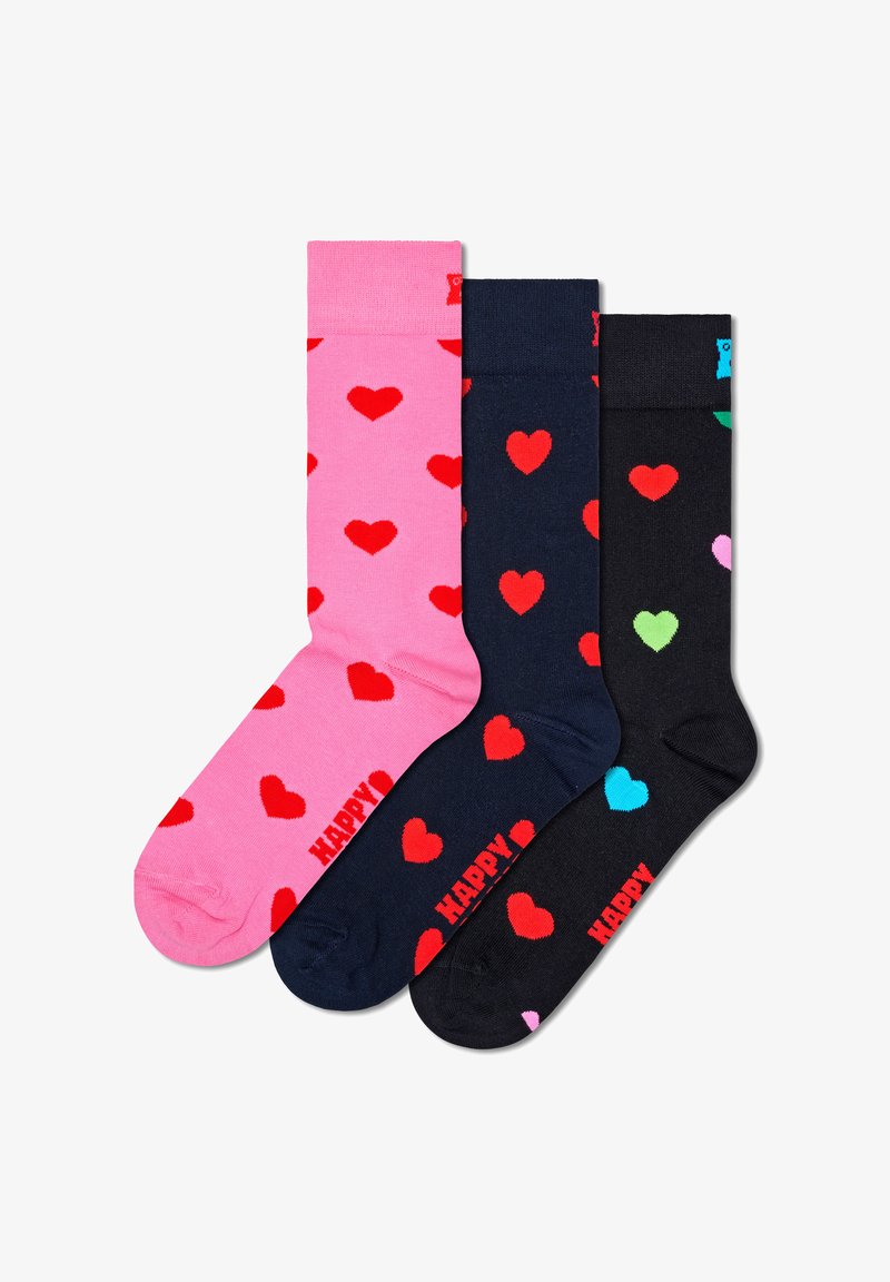 Trois paires de chaussettes en coton. La première est rose avec des cœurs rouges ; la deuxième est bleu marine avec des cœurs rouges ; la troisième est noire avec des cœurs multicolores.