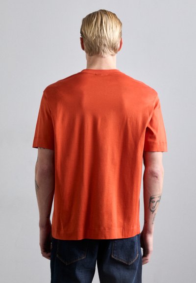 T-shirt à manches courtes et col rond en coton orange vif. Texture lisse avec une coupe décontractée, présentant un ourlet droit et des détails minimes.
