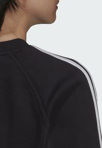 Svart sweatshirt med ribbad textur, med vita sidosträck och raglanärmdesign. Synlig krage och axelsömdetalj.