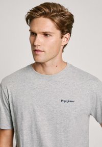 Pilkas medvilnės marškinėliai su apvalia iškirpte ir trumpomis rankovėmis, ant kairiojo krūtinės yra mažas mėlynas "Pepe Jeans" logotipas.