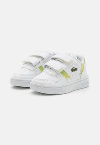 Baskets blanches avec deux bandes Velcro, accents verts et jaunes, tige en cuir texturé, col rembourré et semelle en caoutchouc plate.