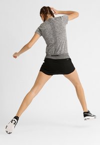 Camiseta atlética gris de manga corta y tejido texturizado, combinada con una falda negra. Zapatillas deportivas en blanco y negro con una suela estampada.