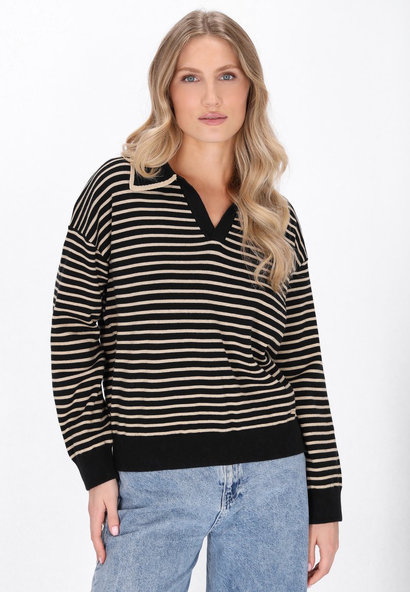 Suéter de rayas negro y beige de manga larga con escote en V y puños acanalados, combinado con jeans de tiro alto en un tono azul claro.