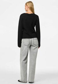 Melna adīta džemperis ar garām piedurknēm, v-veida kakla izgriezums aizmugurē. Saskaņots ar gaismas pelēkiem platām biksēm, kas ir ar aizmugurējām kabatām un brīvu piegriezumu.