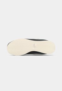 Sort sneakersål med en struktureret, hvid gummioverflade, der har et fiskebensmønster og et prægaftryk af et logo nær hælen.