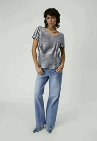 Striped v-neck t-shirt in navy and white, paired with light blue wide-leg jeans. Model stands confidently against a neutral background.