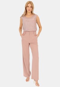 Jasnoróżowe spodnie o szerokich nogawkach o dopasowanym kroju i z kieszeniami, zestawione z błyszczącą, teksturowaną górą w delikatnym różu. Minimalistyczny design, bez wzorów.