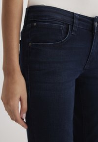 Dark blue denim jeans with a close-fitting design, featuring five pockets and metal accents at the waist and pocket edges.