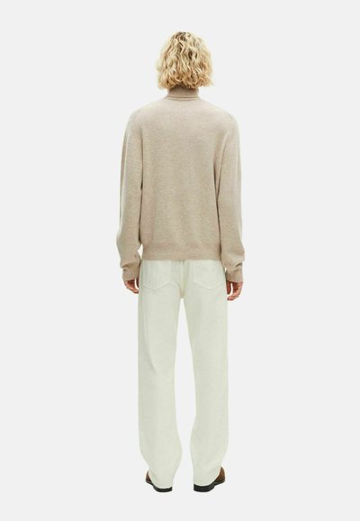 Maglione beige lavorato a maglia con collo alto, abbinato a pantaloni bianchi a gamba larga. Texture morbida, design con spalle cadenti e polsini a coste.