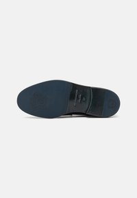 Semelle de chaussure en cuir noir avec une finition lisse, arborant une empreinte de logo et des accents texturés près des zones du talon et des orteils.