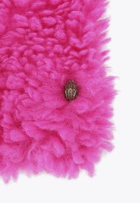 Tissu texturé rose vif avec des touffes moelleuses, comportant un bouton métallique décoratif ressemblant à une fleur ou une feuille intégré dans le matériau.