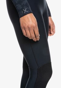 Zwarte wetsuitbroek met een gestructureerd palmenbladpatroon op de manchetten, verstevigd kniegedeelte en flatlock-stiksels voor duurzaamheid en flexibiliteit.