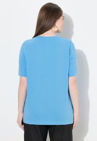 Sininen lyhythihainen toppi, joka on valmistettu pehmeästä, teksturoidusta kankaasta. Siinä on pyöreä kaula-aukko ja rento istuvuus, sekä puhdas, yksinkertainen muotoilu ja helma.