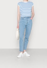 Camiseta a rayas azul claro y blanca con escote amplio, combinada con unos vaqueros de tiro alto en azul claro. Zapatillas blancas y un bolso texturizado completan el look.