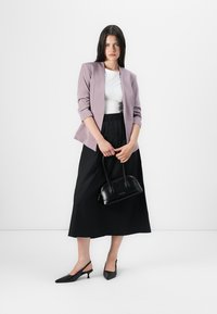 Blazer ajustado morado sobre una blusa blanca, combinado con una falda maxi negra. Los accesorios incluyen un bolso pequeño negro y bailarinas negras de punta.