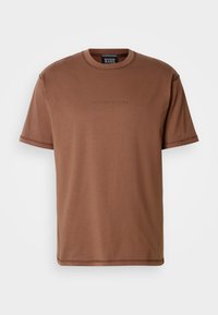 Smeđi pamučni T-shirt s okruglim izrezom, kratkim rukavima i suptilnim brandingom na prsima. Glatka tekstura i opušteni kroj.