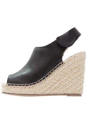 Sandale compensée en cuir noir avec bout fermé, semelle plateforme en corde tressée et bride de cheville réglable avec fermeture Velcro.