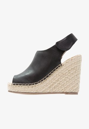 Sandalia cuña de cuero negro con puntera cerrada, suela plataforma de cuerda tejida y correa ajustable en el tobillo con cierre de velcro.