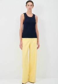 Top senza maniche di colore blu navy con scollatura rotonda, decorato con borchie argentate lungo le spalle. Abbinato a pantaloni a gamba larga gialli con vita alta.