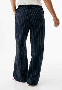 Granatowe, szerokie spodnie w paski o miękkiej fakturze, charakteryzujące się luźnym krojem, elastycznym pasem i delikatnymi kontrastującymi prążkami.