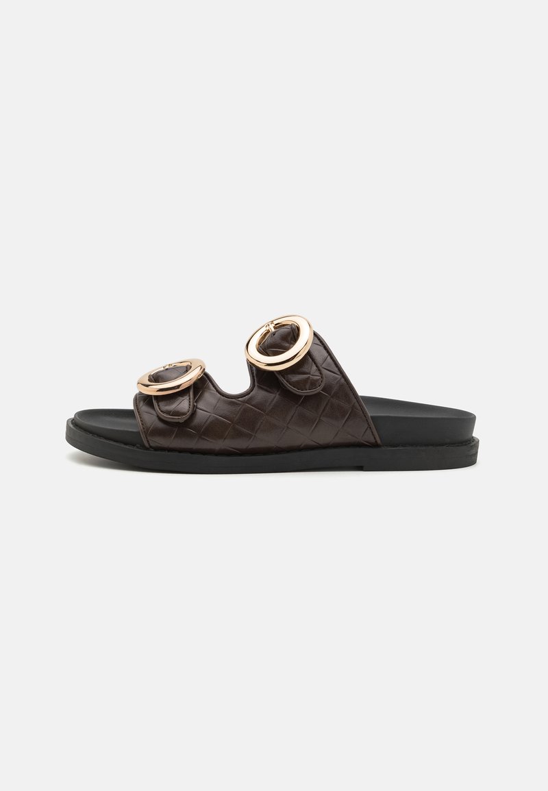 Sandales à glissière matelassées marron avec deux accents dorés circulaires sur le dessus. Semelle intérieure lisse noire et semelle extérieure en caoutchouc durable.