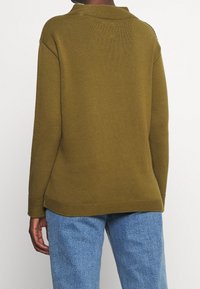 Maglione verde oliva a costine con vestibilità rilassata, colletto rotondo e spalle scese. Abbinato a jeans in denim blu chiaro.