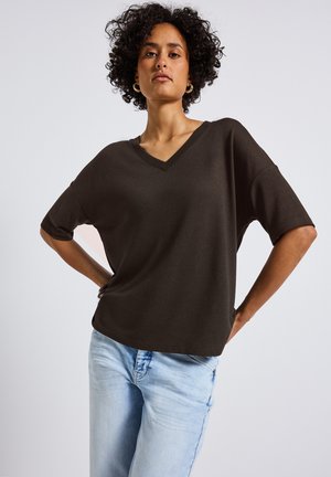 Bruine V-hals oversized T-shirt met korte mouwen, gemaakt van zachte stof. Gecombineerd met lichtblauwe denim jeans, die een comfortabele pasvorm benadrukken.