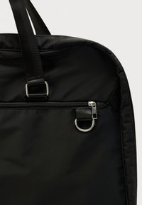 Geantă din nailon negru cu fermoar superior, elemente metalice argintii și mânere țesute rezistente. Textură netedă, design structurat.