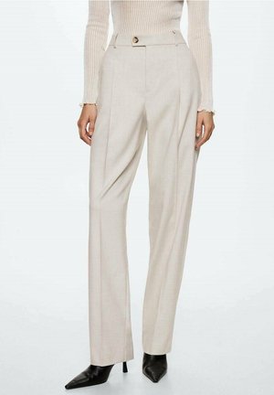 Beige, hooggetailleerde, op maat gemaakte broek met voorplooien, gecombineerd met zwarte, puntige, met hakken uitgevoerde laarzen en een crèmekleurige, geribbelde, lange mouwen top.