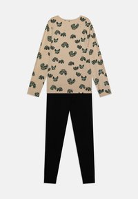 Beige Langarmshirt mit grünem und schwarzem Kakteenmuster; kombiniert mit schwarzen, enganliegenden Leggings mit umgeschlagenen Säumen. Schlichtes, lässiges Design.