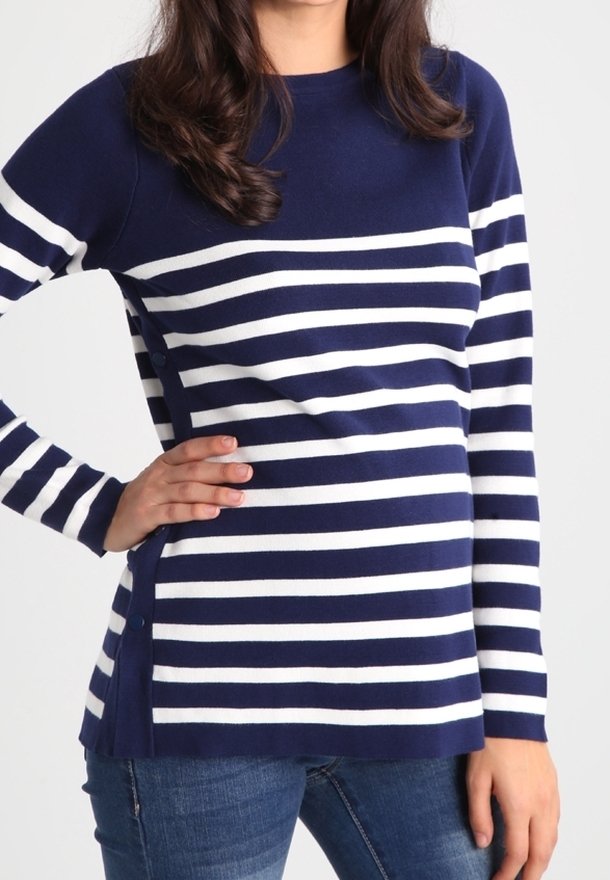 Femme portant un pull à manches longues à rayures horizontales bleu marine et blanches avec des boutons sur le côté, associé à un jean bleu.