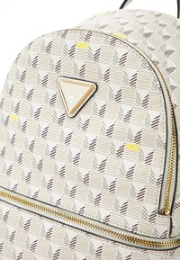 Sac à dos blanc avec un motif géométrique en gris, or et noir, doté d'une fermeture éclair dorée et d'une plaque logo à l'avant.