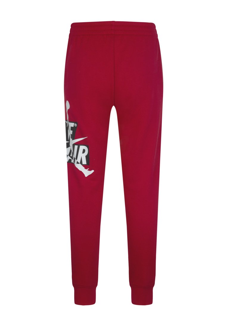 Pantalones de chándal rojos con cintura y puños elásticos, que presentan un logo de Nike Air en blanco y negro y la silueta del Jumpman en el muslo izquierdo.