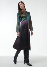 Lang, kleurrijke jurk met een geometrisch patroon; heeft lange mouwen en een zijdeachtige textuur, aangevuld met kniehoge zwarte laarzen.