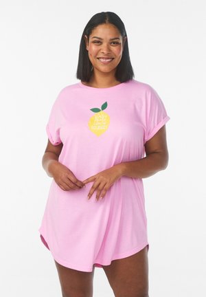 Kvinde smilende iført en løs lyserød kjole med op rullede ærmer og en citrongrafik på brystet, hvor der står "Easy Peasy Lemon Squeezy".