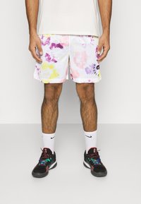 Weiße Mesh-Shorts mit mehrfarbigen abstrakten Mustern in Pink, Lila und Gelb. Kombiniert mit schwarzen Turnschuhen und weißen Nike-Socken.
