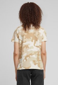 T-shirt camouflage beige con maniche corte, scollatura rotonda e tessuto morbido; progettato per un abbigliamento casual.