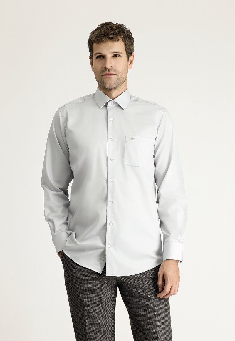 Camicia button-up a maniche lunghe grigia chiara con colletto strutturato, taschino sul petto e texture del tessuto liscia, abbinata a pantaloni grigi con fantasia.