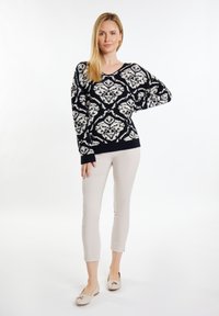 Pulover negru din tricot cu un model floral alb, decolteu în V și mâneci lungi. Asortat cu pantaloni bej slim-fit și pantofi plate de culoare deschisă.